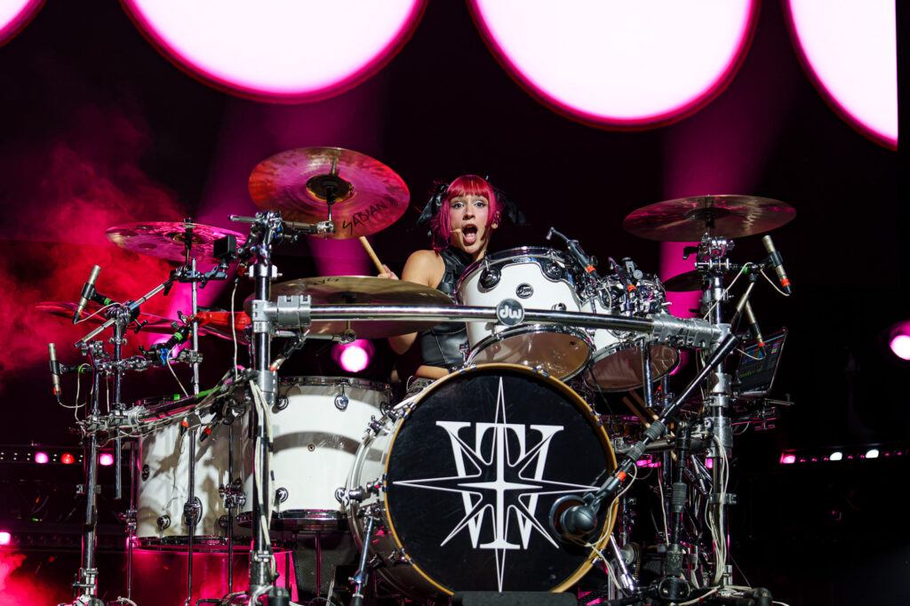 The-Warning-The-Fonda-Theater-Zharmaine-Boatman-The-824-Journal-8 – The 824 Journal The Warning at The Fonda Theatre in Los Angeles: drummer with pink hair performs on a white drum kit under pink stage lights, mid-song with sticks raised.