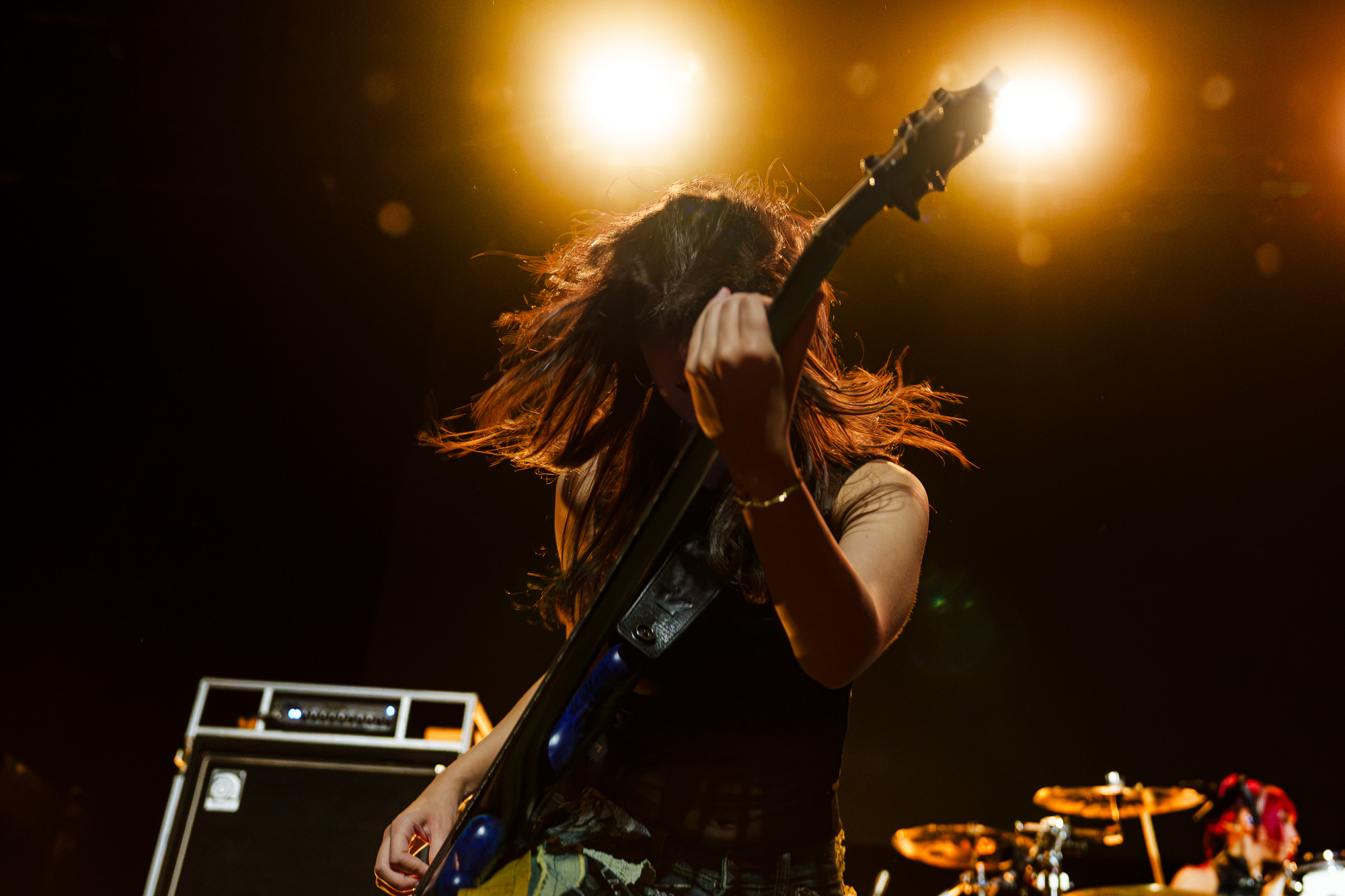 The Warning guitarist playing a blue electric guitar under bright stage lights at The Fonda Theatre in Los Angeles.