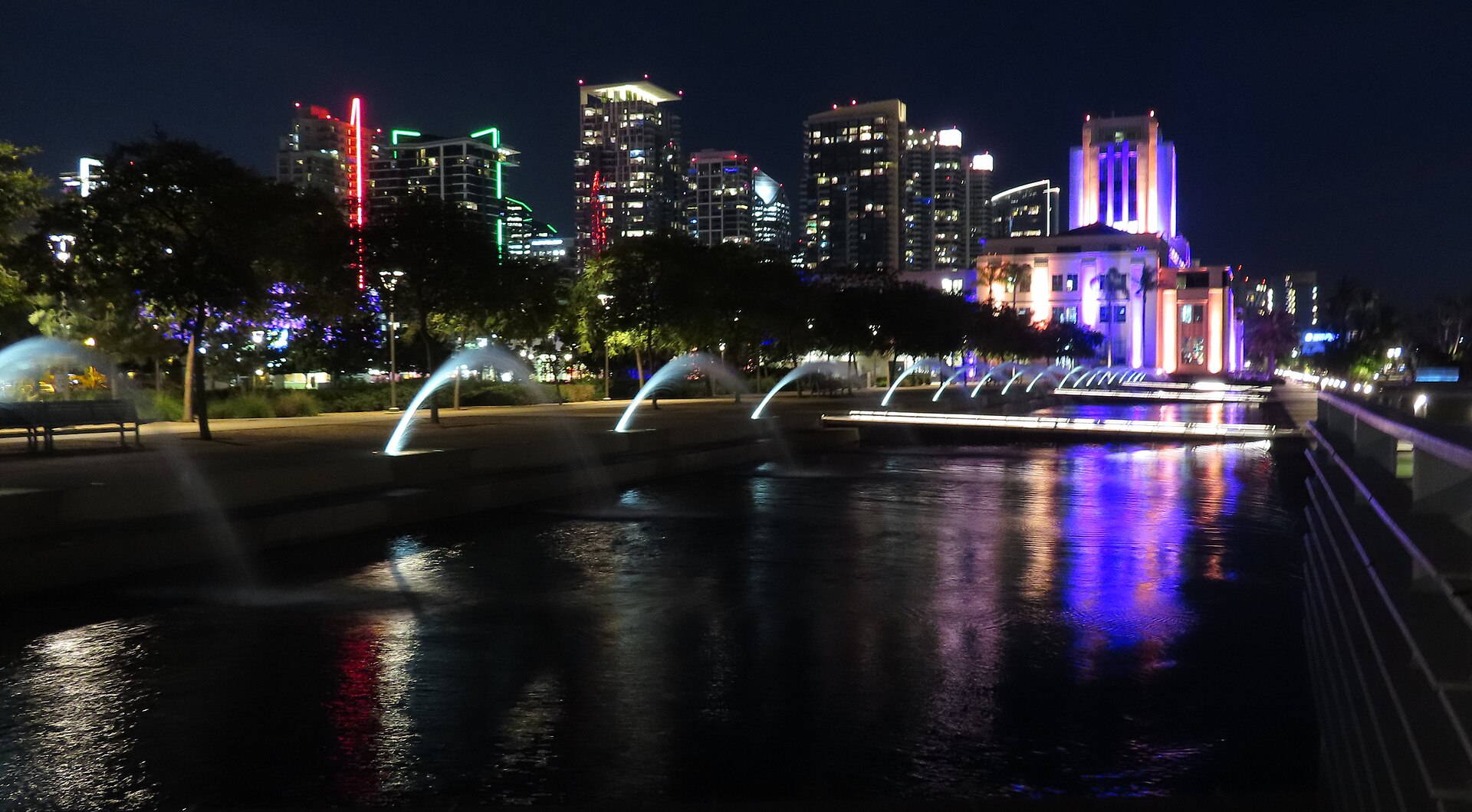 Waterfront Park in San Diego at night, with lit fountains in the reflecting pool, the County Administration Center glowing purple, and downtown towers behind