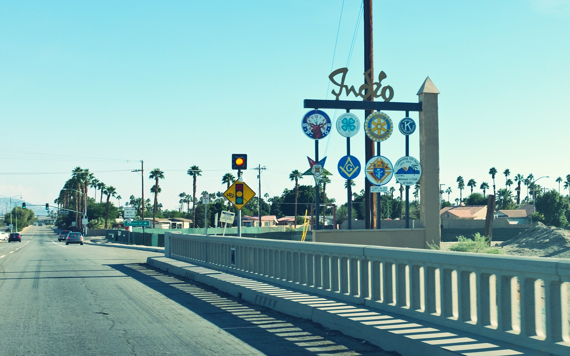 A tall welcome sign at the entrance to Indio, California, beside a road under a clear blue sky