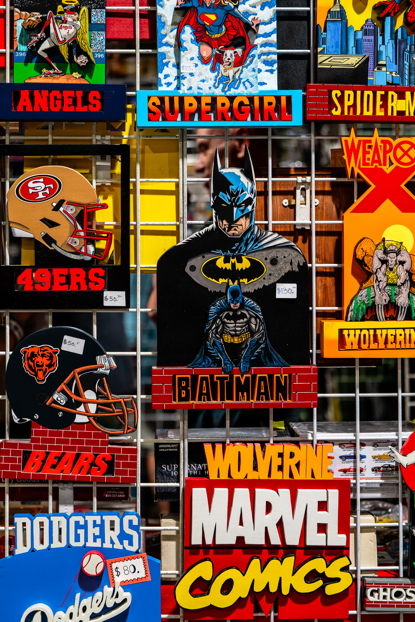 Bright wall of comic signs and cutouts featuring Batman centerpiece with surrounding logos like Marvel, Spider-Man, Wolverine, and Superman/Supergirl themes.