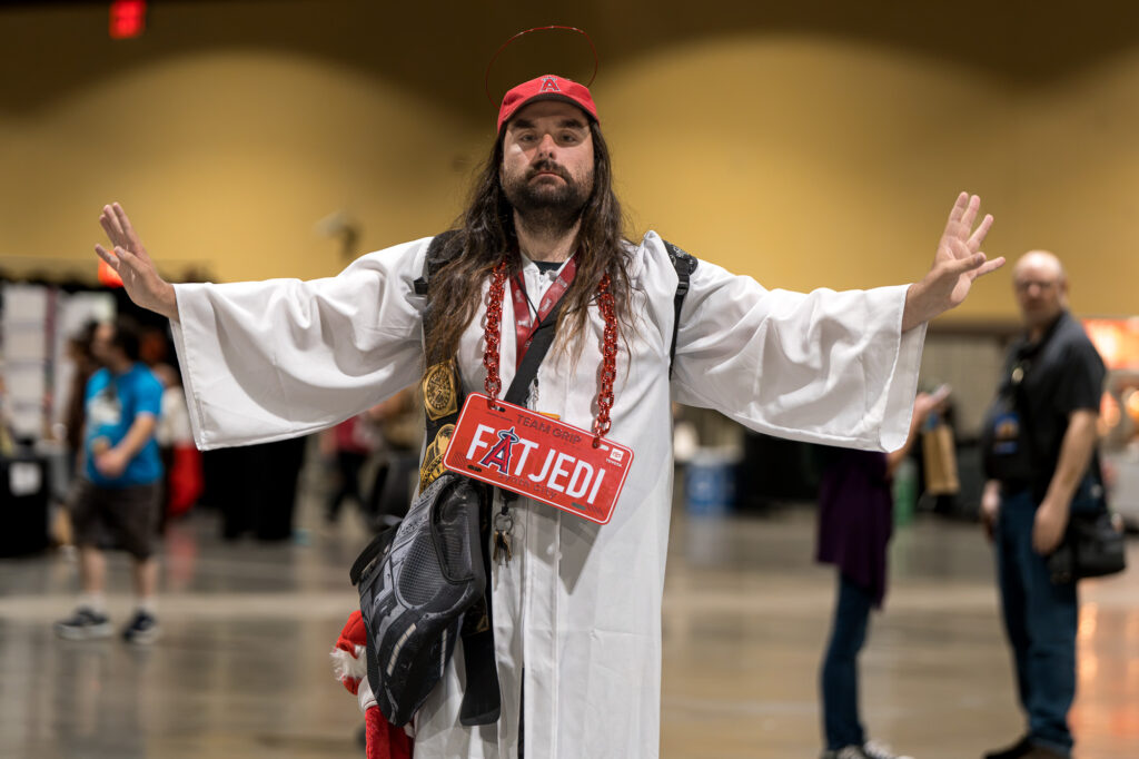 Zharmaine-Boatman-Long-Beach-Comic-Con-the8244journalpress-46894 – The 824 Journal Long Beach Comic Con 2026: man in a white robe with long hair and halo-like headpiece poses with arms outstretched at a convention.