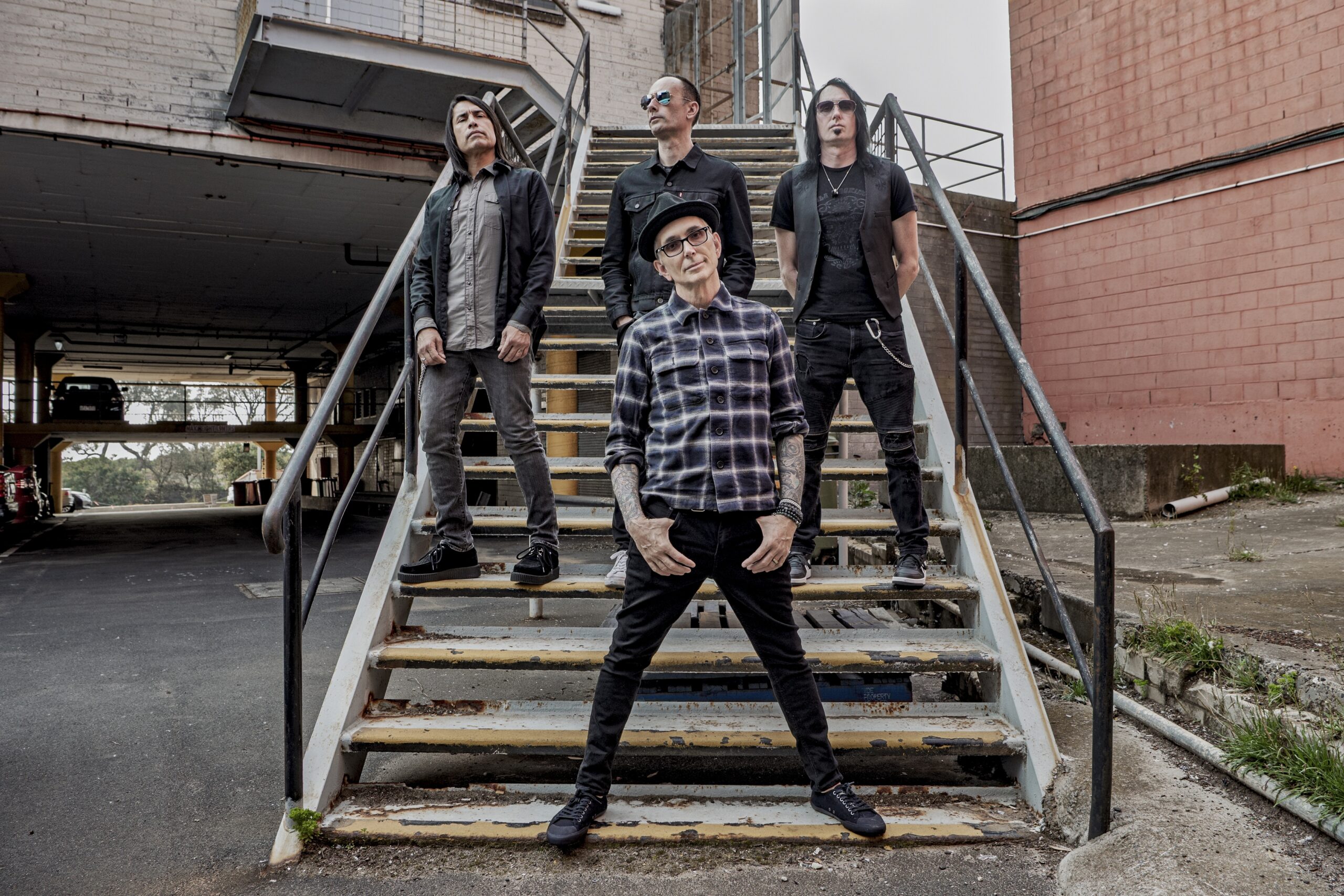 Everclear's four members posed on an outdoor metal staircase, Art Alexakis in front wearing a hat and plaid shirt