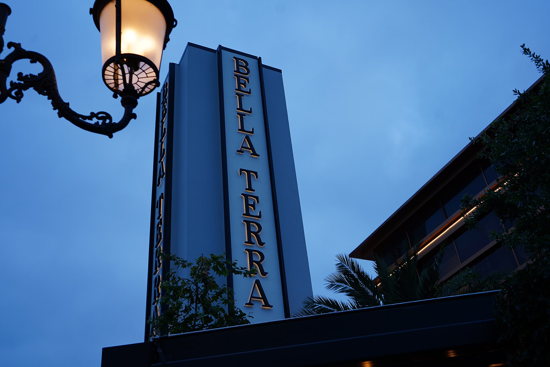 The Bella Terra sign tower and a decorative street lamp against a blue evening sky in Huntington Beach