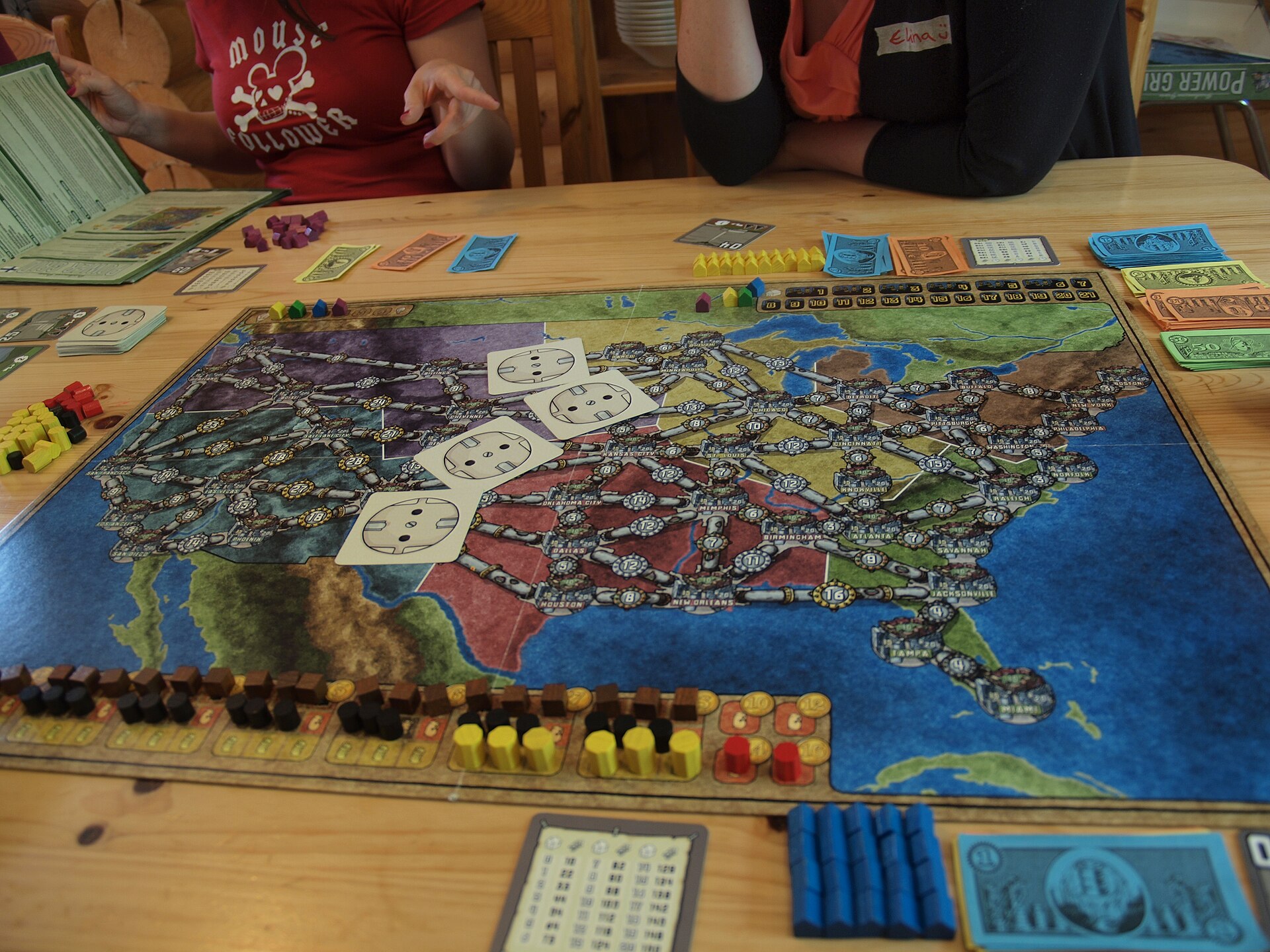 A Power Grid game board covered in colored houses, resource tokens, and power plant cards mid-game