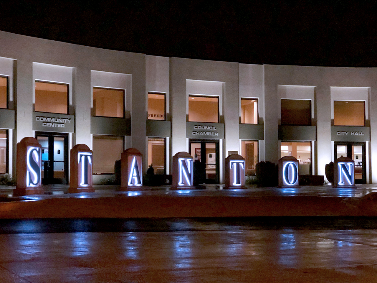 Lighted STANTON letters in front of Stanton City Hall at night, reflected on wet pavement after rain