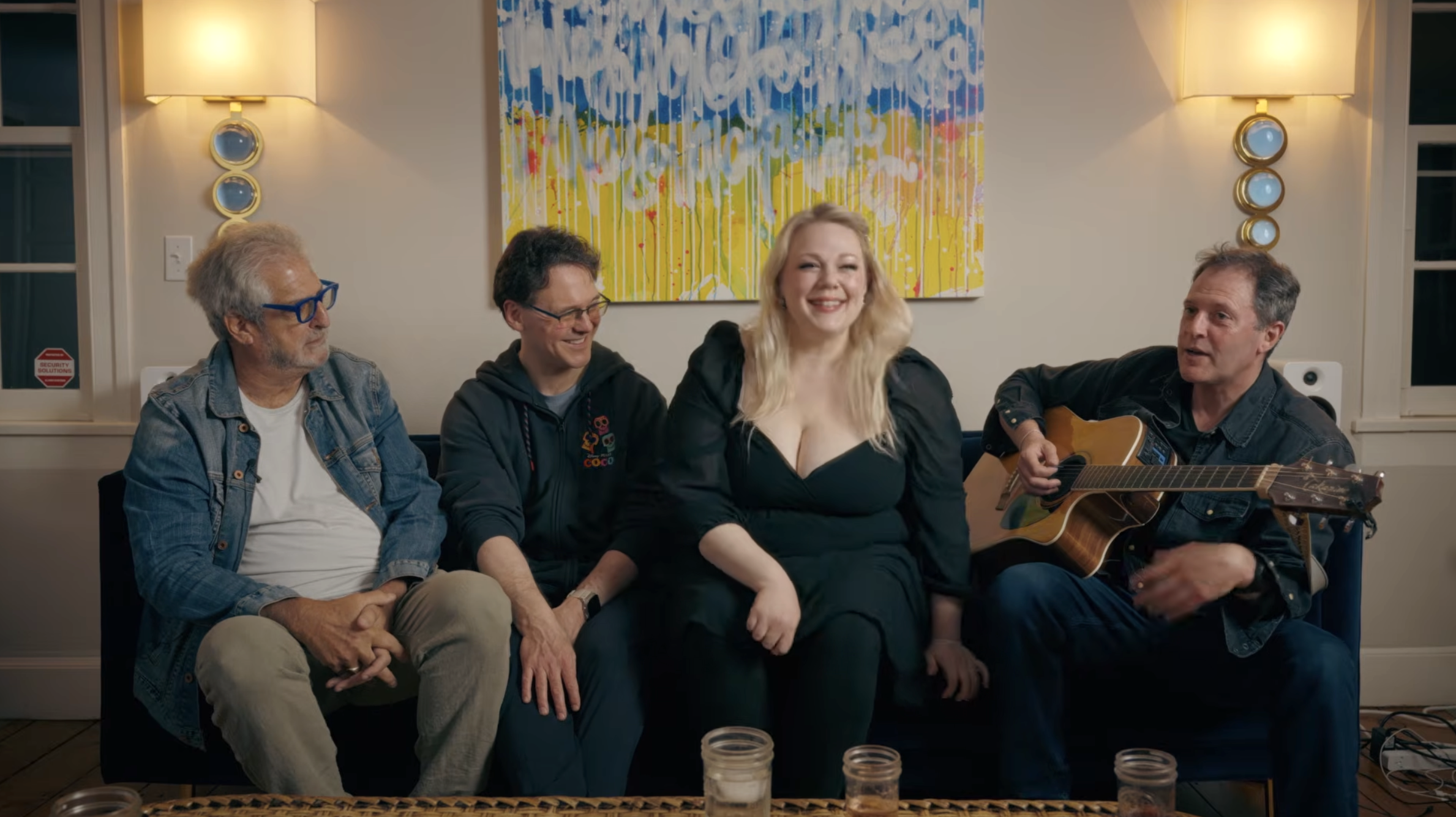 Four members of The Give seated on a couch, one playing acoustic guitar